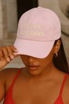 Woman wearing a baby pink Healthy Gal™ dad cap embroidered with "hotties do pilates" in gold lettering