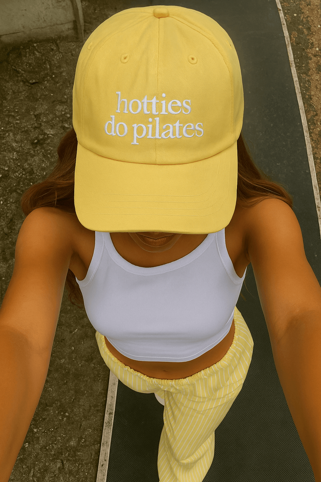 Woman wearing a butter yellow Healthy Gal™ dad cap embroidered with "hotties do pilates" in white lettering, overhead angle