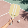 Hand holding a Healthy Gal™ Move pickleball paddle on a pink clay court with a pickleball in mid-air and palm leaf shadows