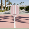Healthy Gal™ Move pickleball paddle in dusty pink standing upright on a clay court with palm trees and a pool in the background