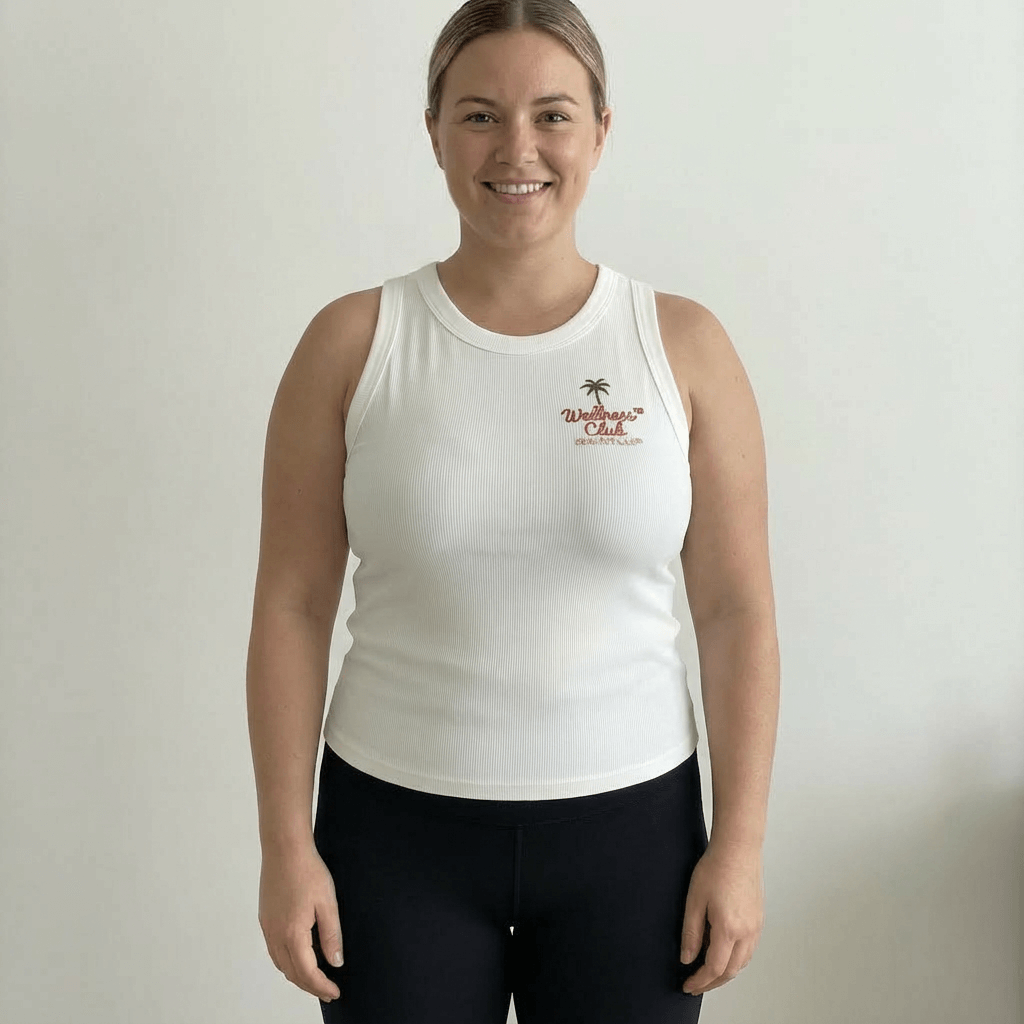 Woman smiling in the Healthy Gal™ Wellness Club Tank in white ribbed fabric with embroidered logo, styled with black leggings, plain background